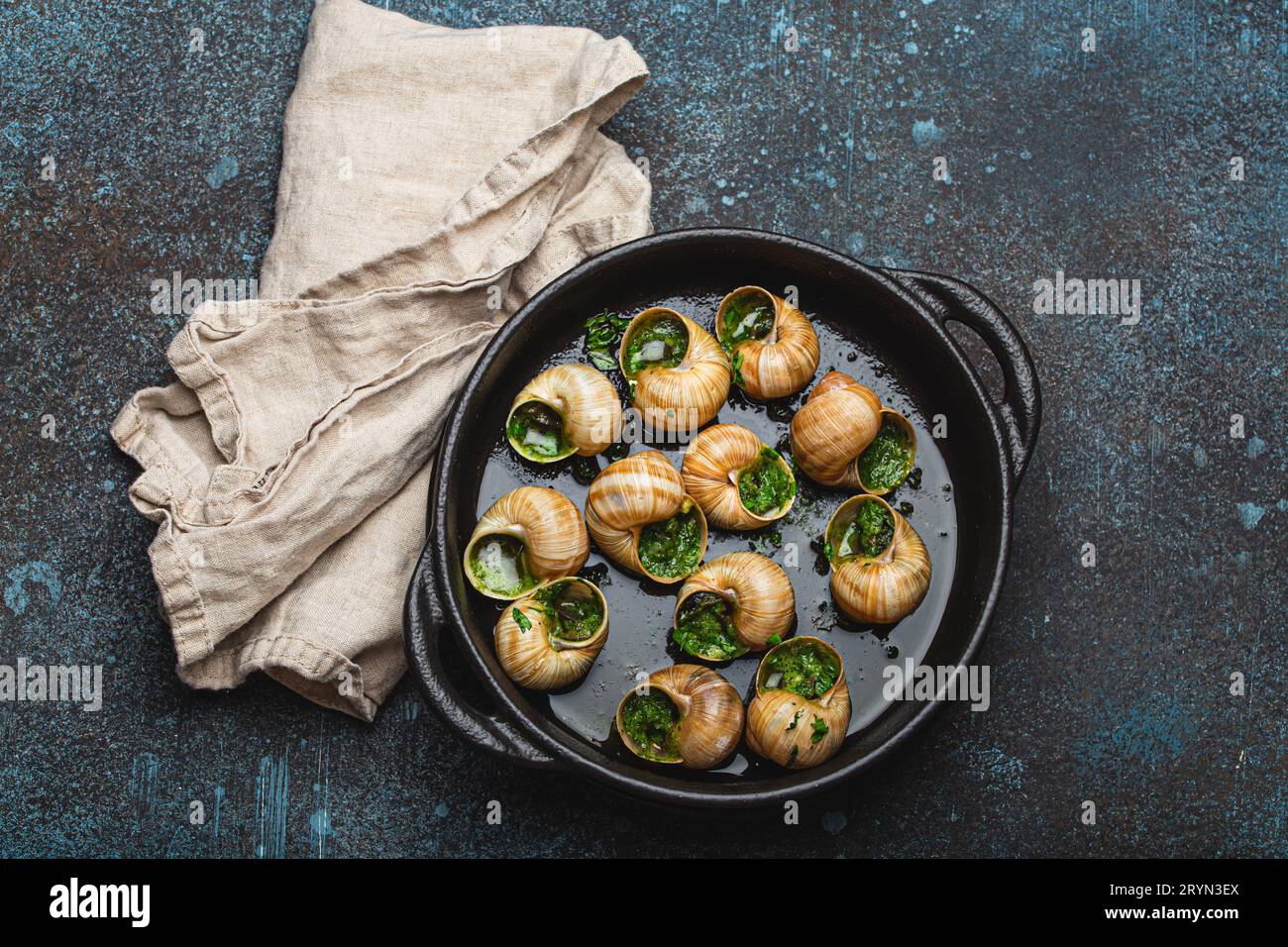 Escargots de Bourgogne Cooked Snails with Garlic Butter and Parsley in black cast iron pan on