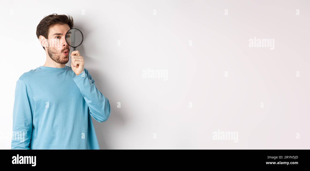 Curious guy looking through magnifying glass on right logo, saying wow, found cool thing, standing on white background Stock Photo