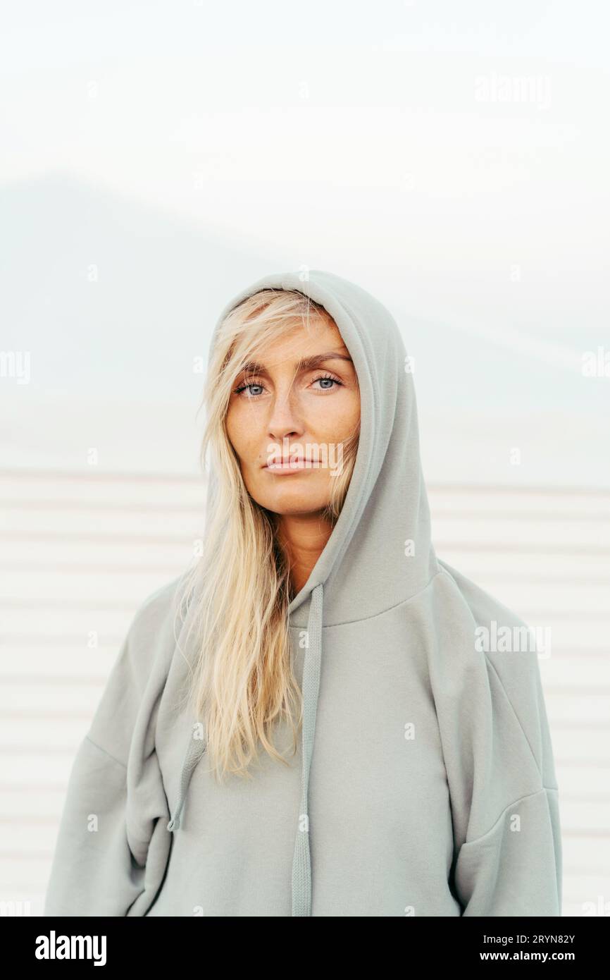 White tanned blond woman thirty year old outside in a gray hoodie. Close-up monochrome vertical portrait of a woman with a Scand Stock Photo