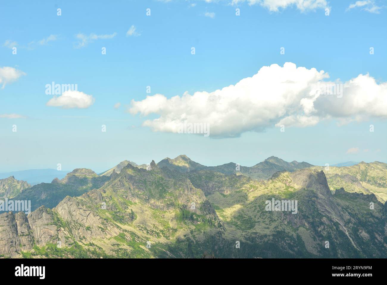 White cumulus clouds casting a shadow float over a rocky massif with pointed peaks on a summer sunny day. Natural park Ergaki, Krasnoyarsk region, Sib Stock Photo