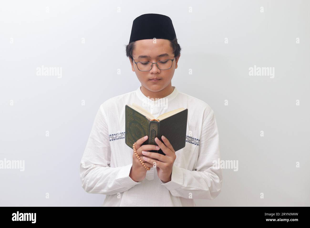 Portrait of young Asian muslim man reading and reciting Holy book of Quran seriously. Isolated image on white background Stock Photo