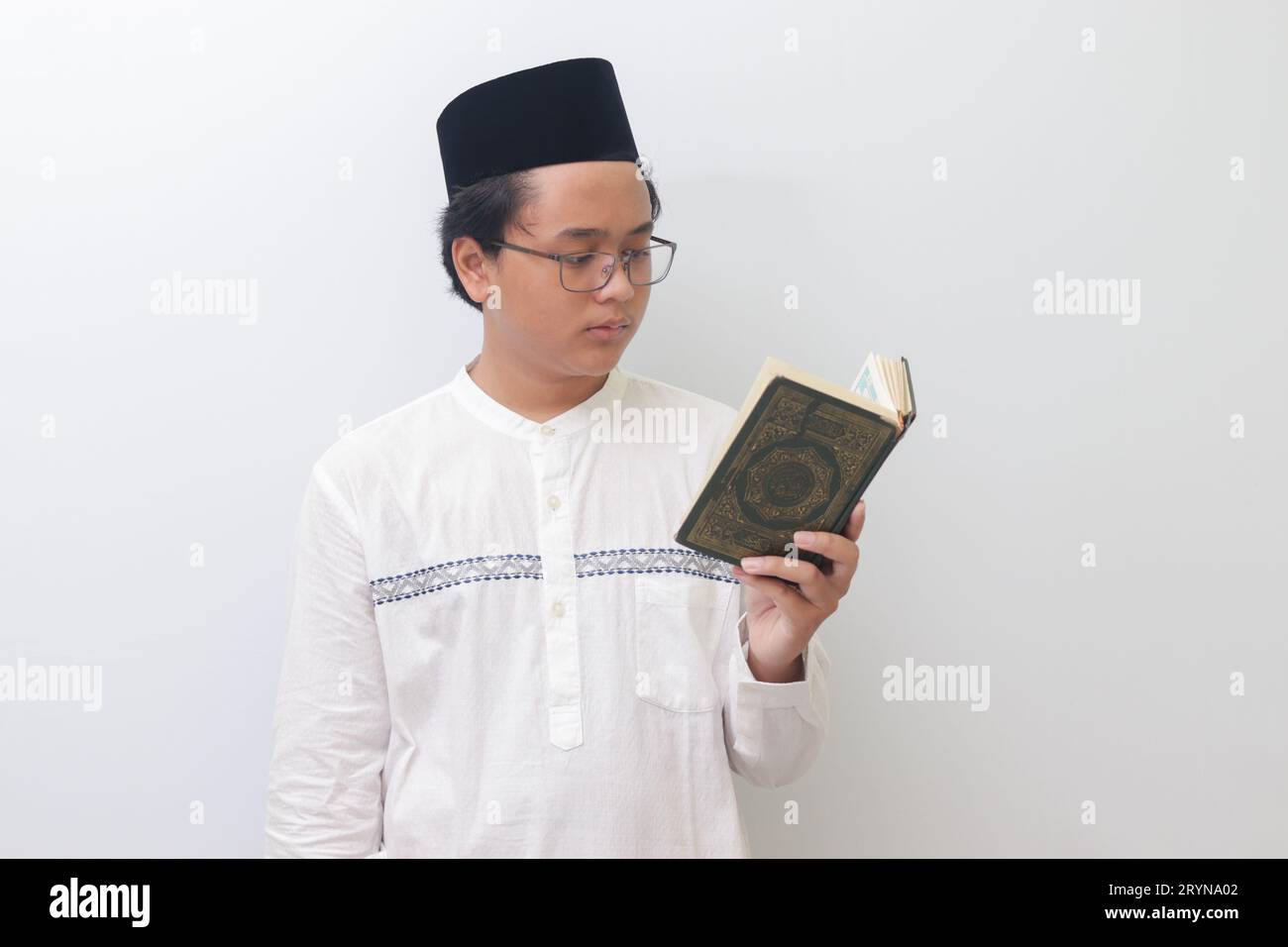 Portrait of young Asian muslim man reading and reciting Holy book of Quran seriously. Isolated image on white background Stock Photo