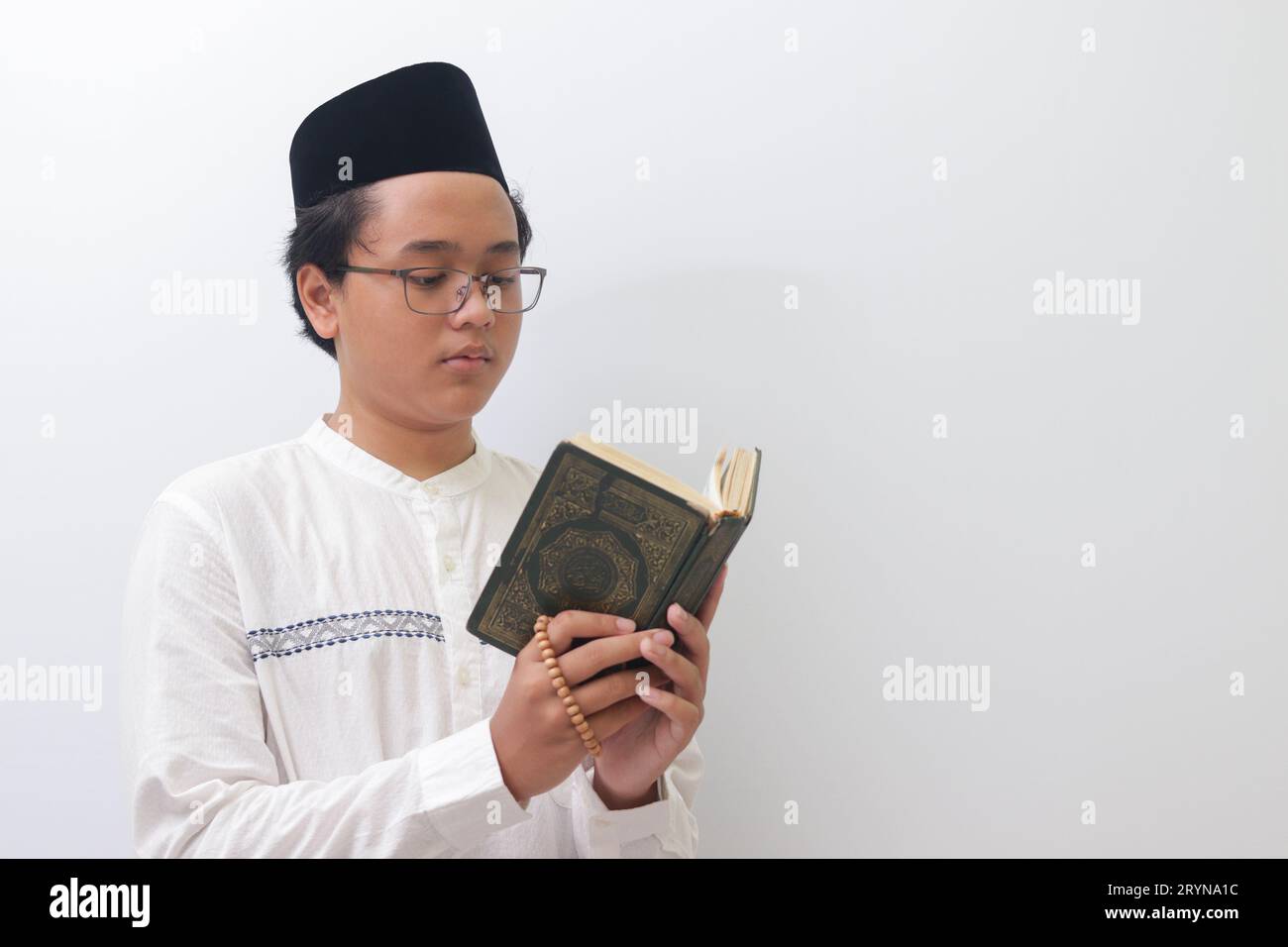 Portrait of young Asian muslim man reading and reciting Holy book of Quran seriously. Isolated image on white background Stock Photo