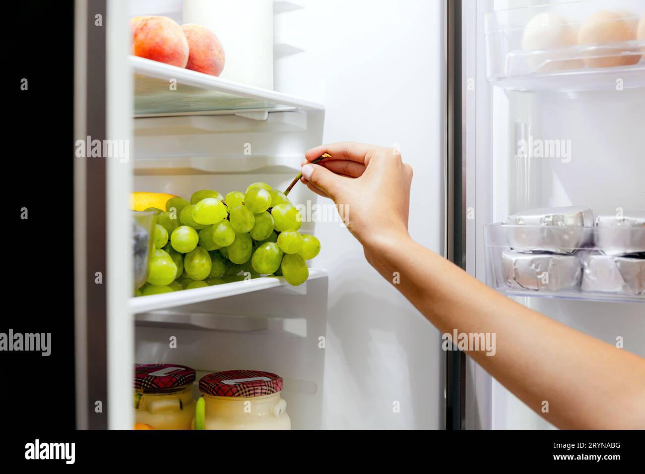 Woman hand taking, grabbing or picks up green bunch of grapes out of