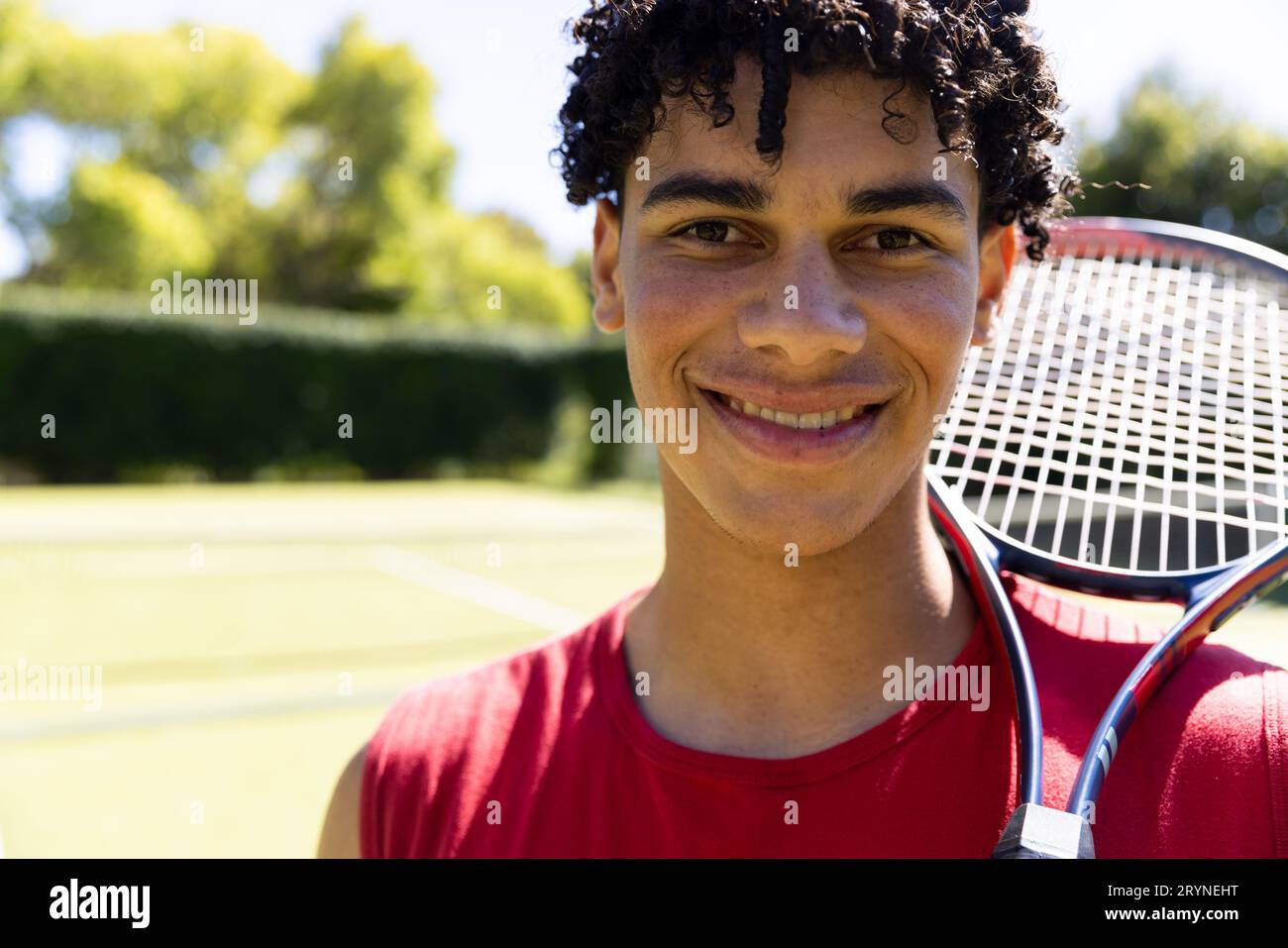 Close-up of biracial young man with tennis racket smiling in tennis court and looking at camera Stock Photo