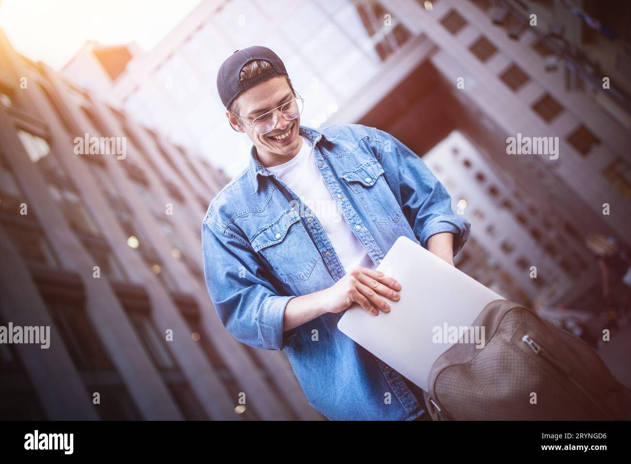 Smart attitude. Positive handsome man using a laptop and sitting in the street while surfing the internet have a web conference. Stock Photo