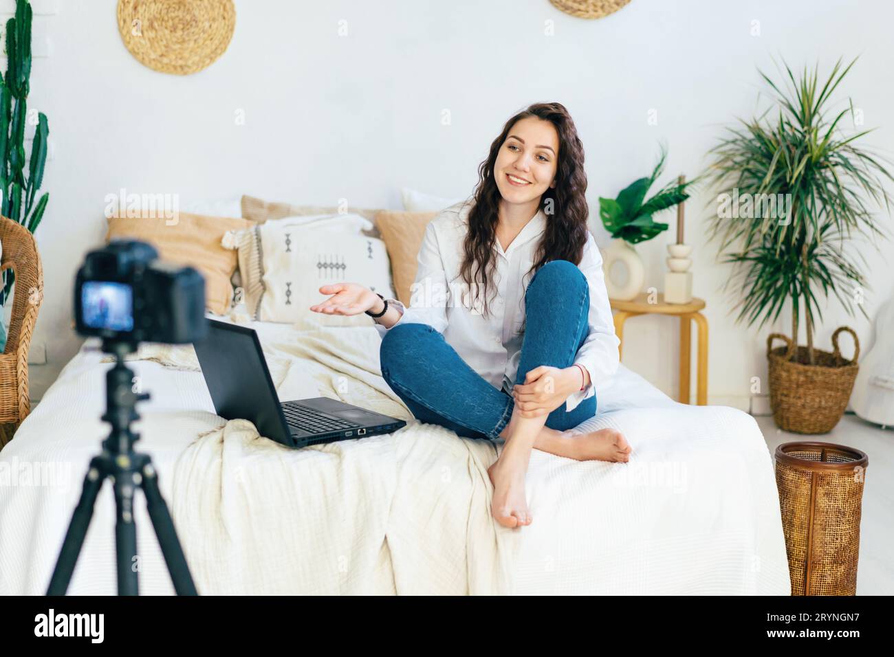 The blogger girl sits on the bed in the bedroom and records a video clip on the camera. Stock Photo