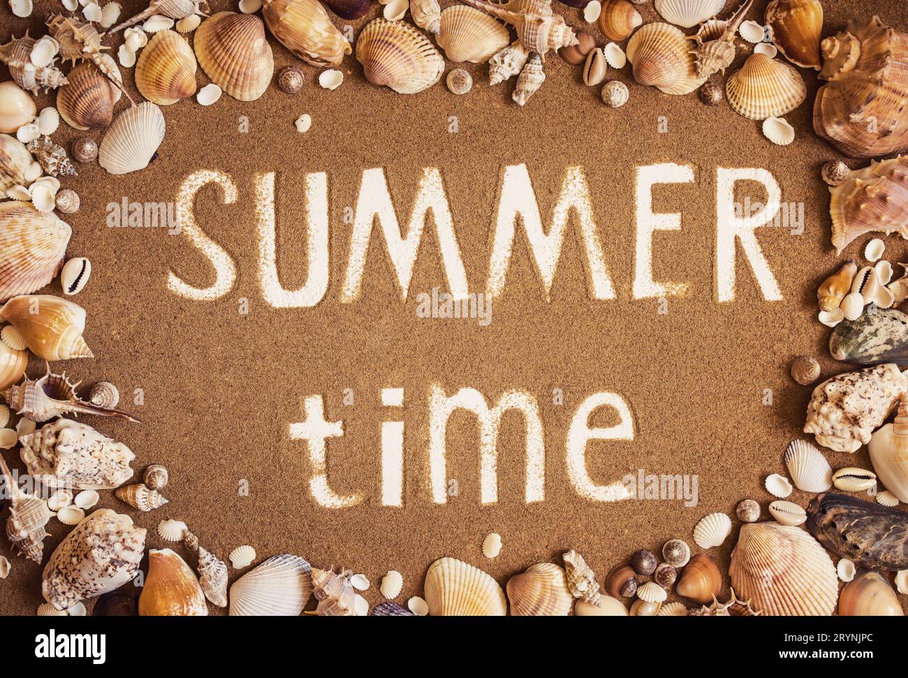 Summer time is written on the sand in frame of sea shells. Trave Stock Photo