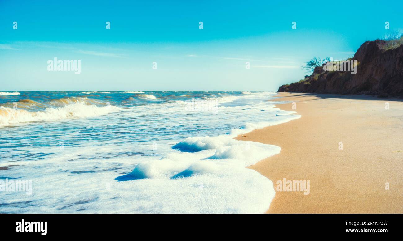 Landscape empty deserted sand beach and sea waves with foam surf with blue sky and white clouds Stock Photo