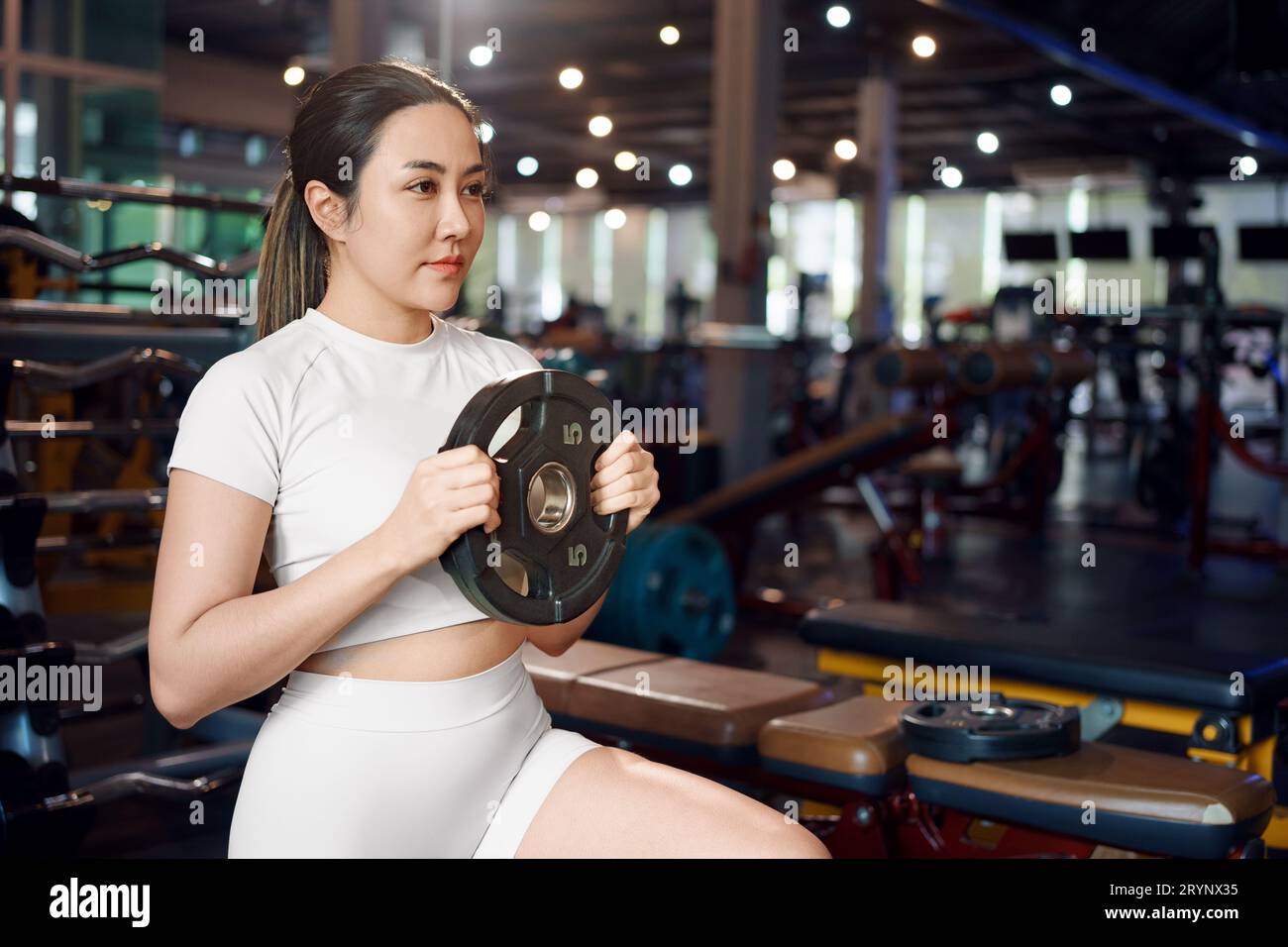 Young asian woman doing exercises with heavy weights plates in gym. Stock Photo