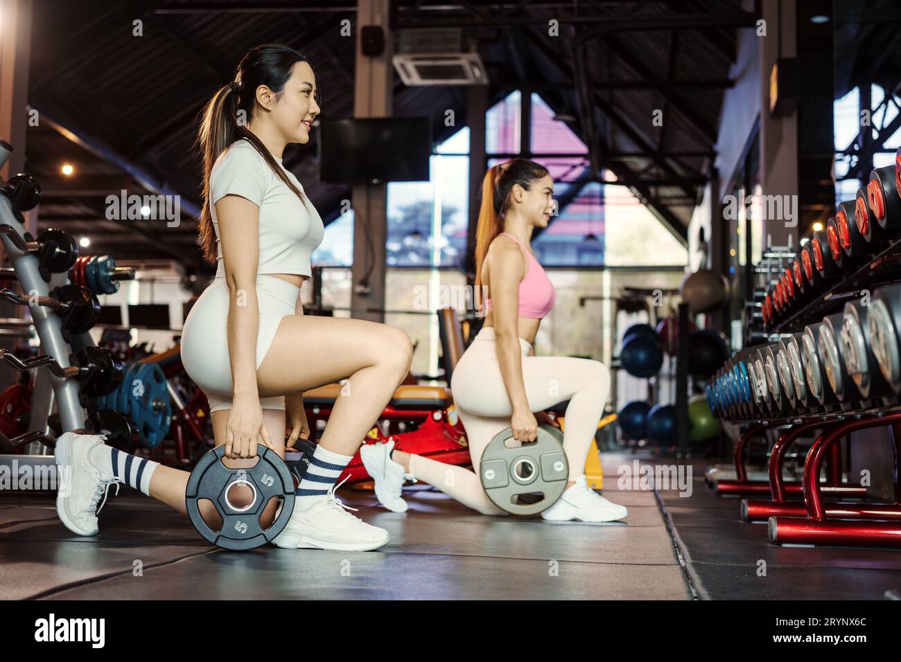 Two young asian woman doing exercises with heavy weights plates in gym. Stock Photo