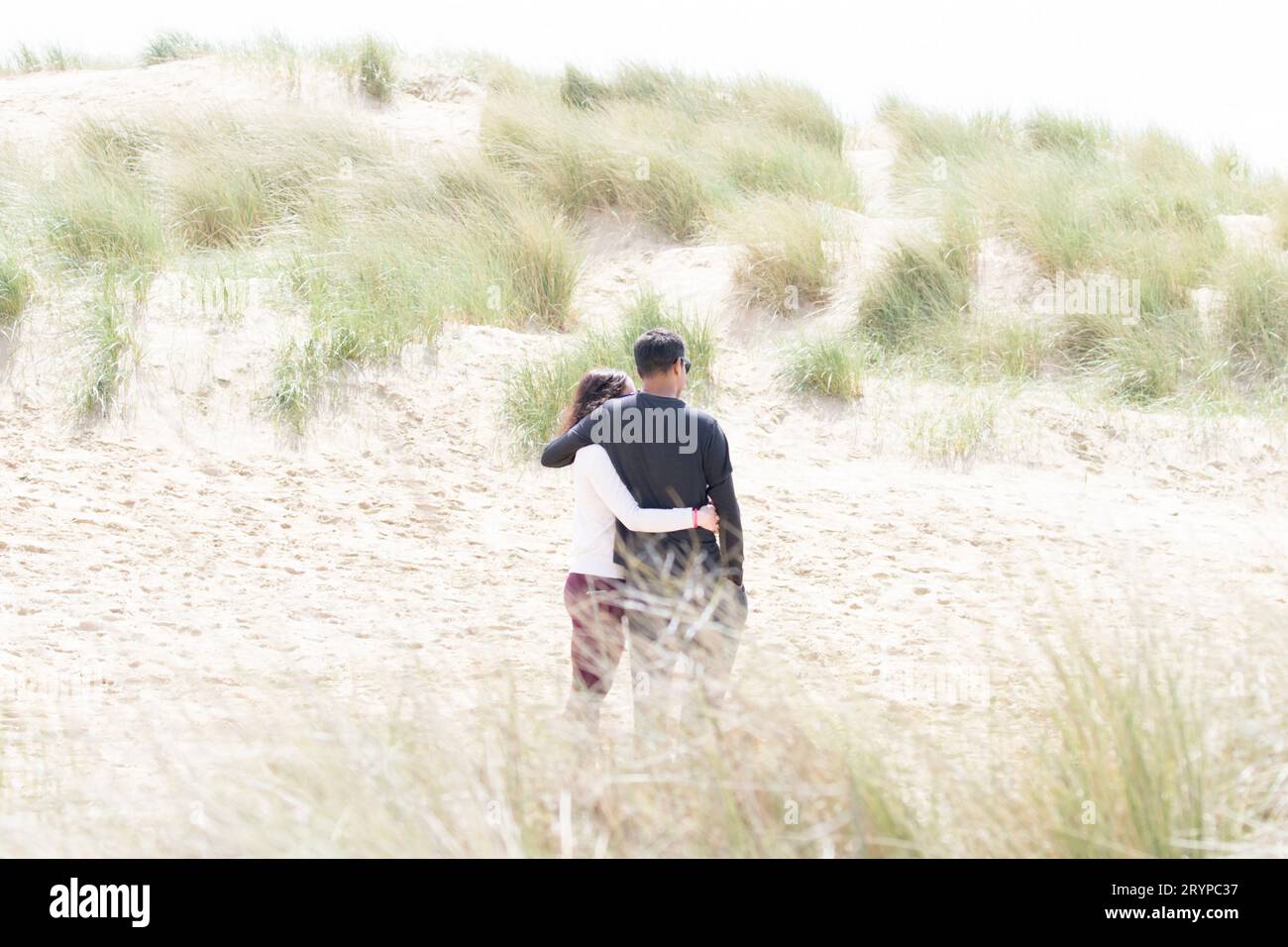 A couple from behind engage in a romantic hug on the sand dunes at ...
