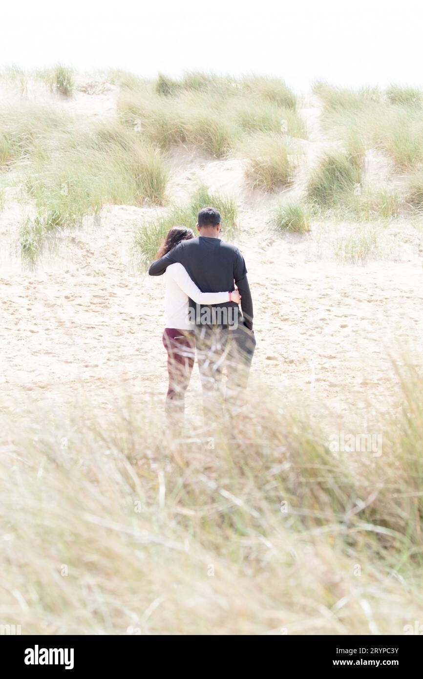 A couple from behind engage in a romantic hug on the sand dunes at ...