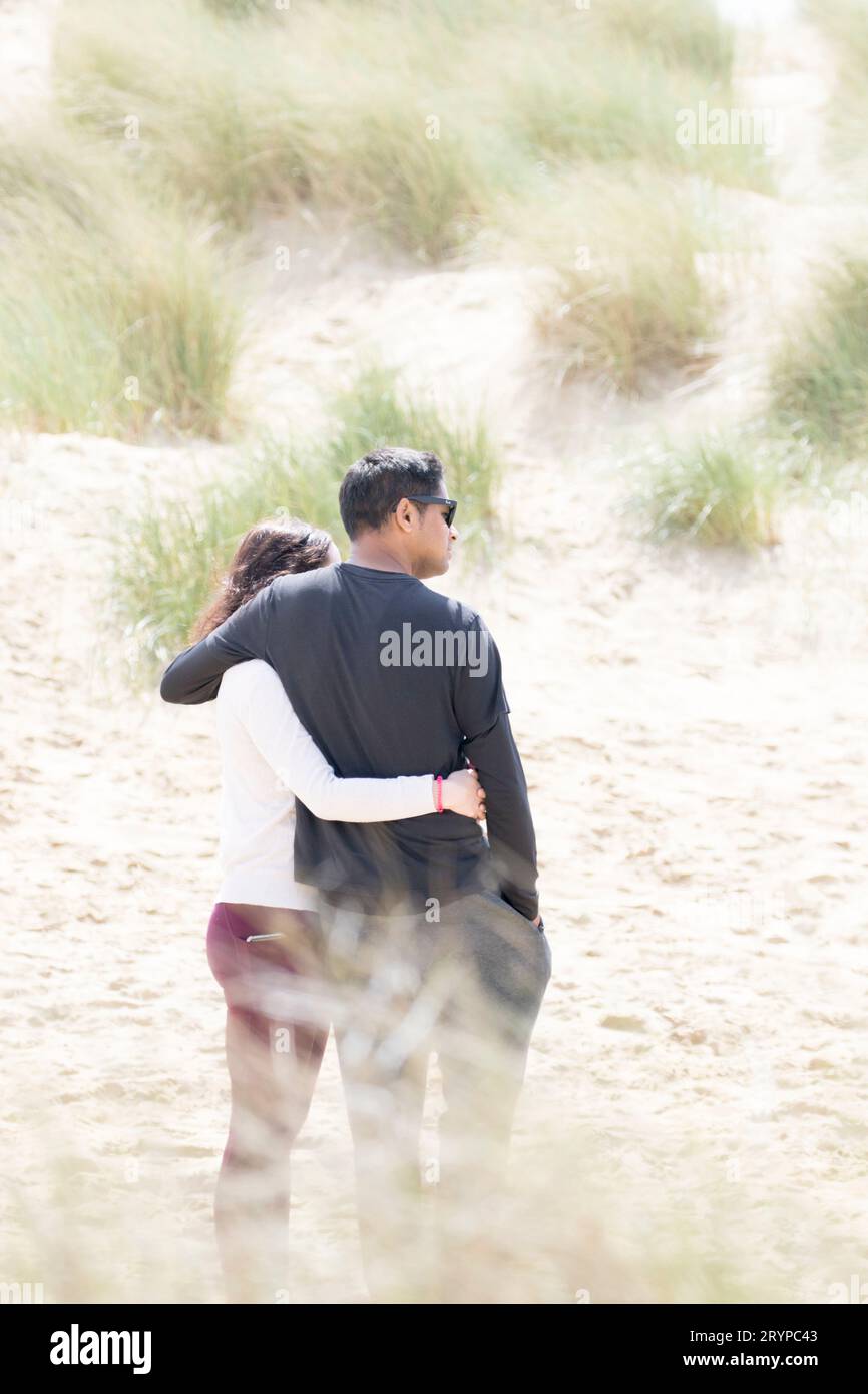 A couple from behind engage in a romantic hug on the sand dunes at ...