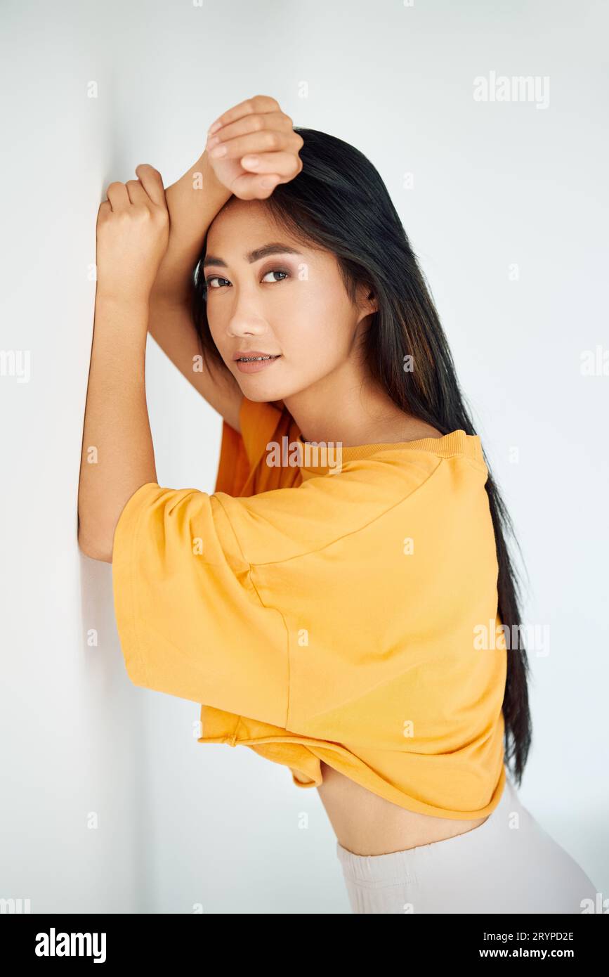 Pretty young asian woman in bright yellow t-shirt posing on white studio background. Female beauty Stock Photo
