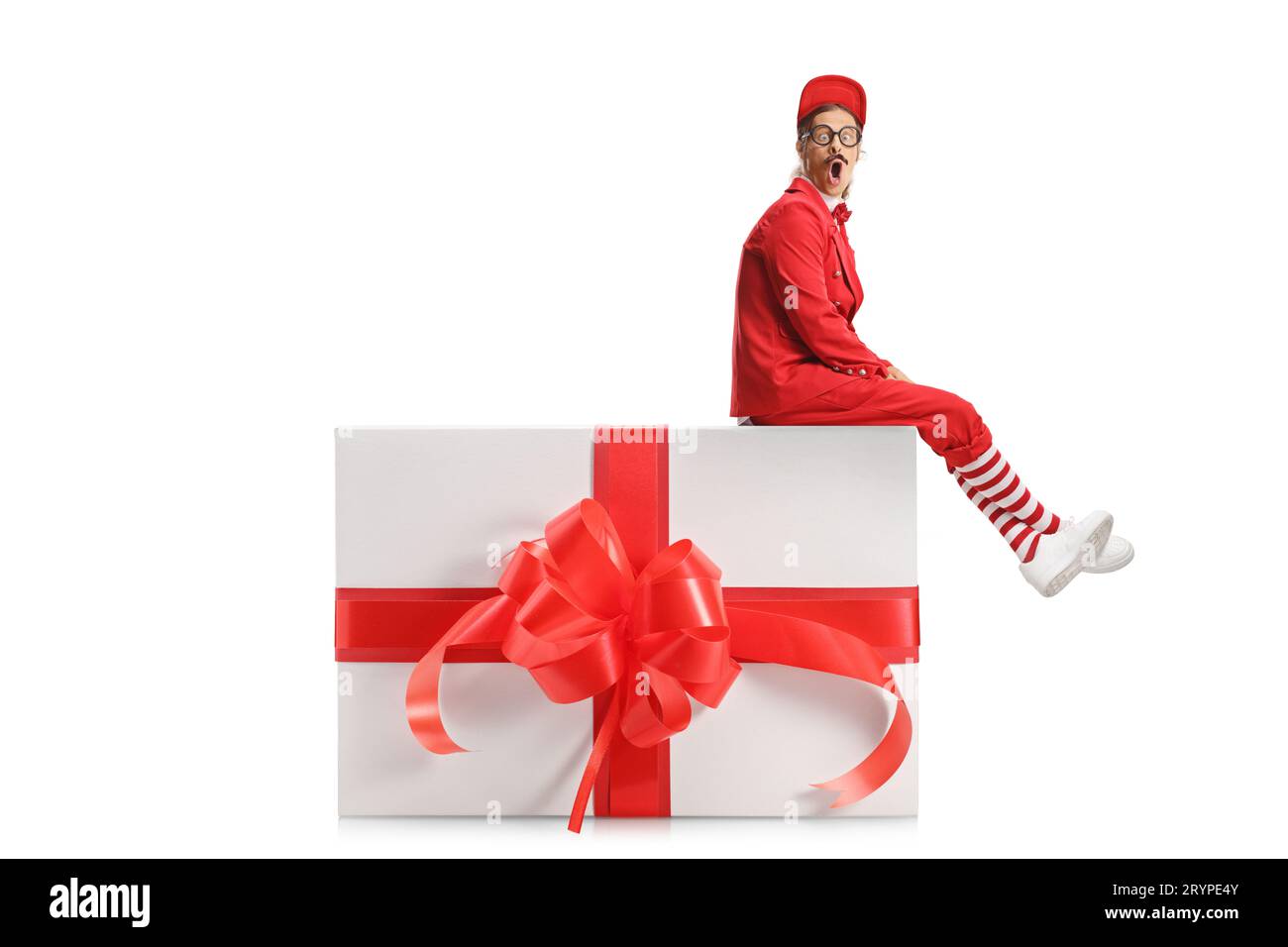 Entertainer in a red suit sitting on a big present box and looking at camera isolated on white background Stock Photo