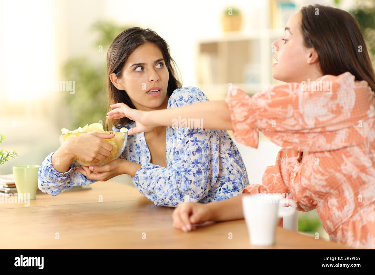 Woman trying to eat potatto chips and selfish friend avoiding at home Stock Photo