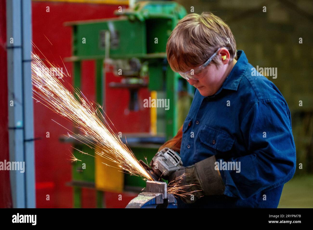 Young high-school boy wearing protective eyewear learning to use an angle grinder in a trade course to teach technical skills Stock Photo