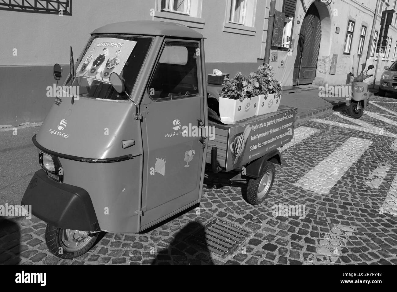 Black and white Heiss and Eis Cafe, smallest coffee shop in Sibiu. Front window for ordering and an auto rickshaw (Tuk tuk) Stock Photo