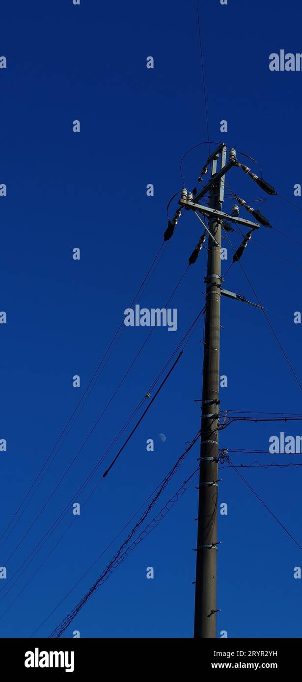 A tall, metal telephone pole stands in the center of the frame with many wires connected to it