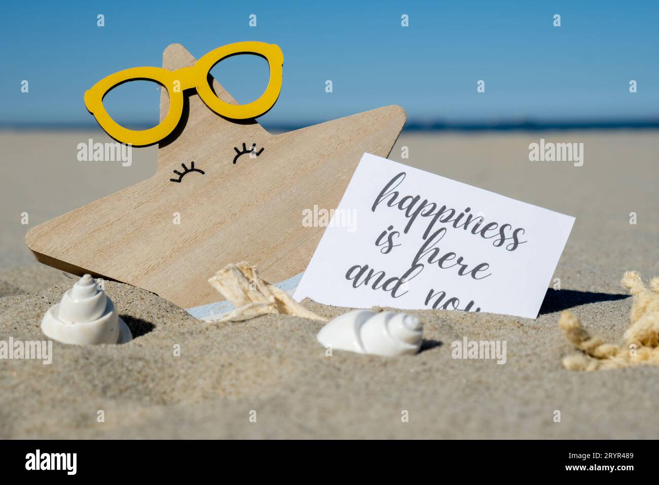HAPPINESS IS HERE AND NOW text on paper greeting card on background of funny starfish in glasses summer vacation decor. Sandy be Stock Photo