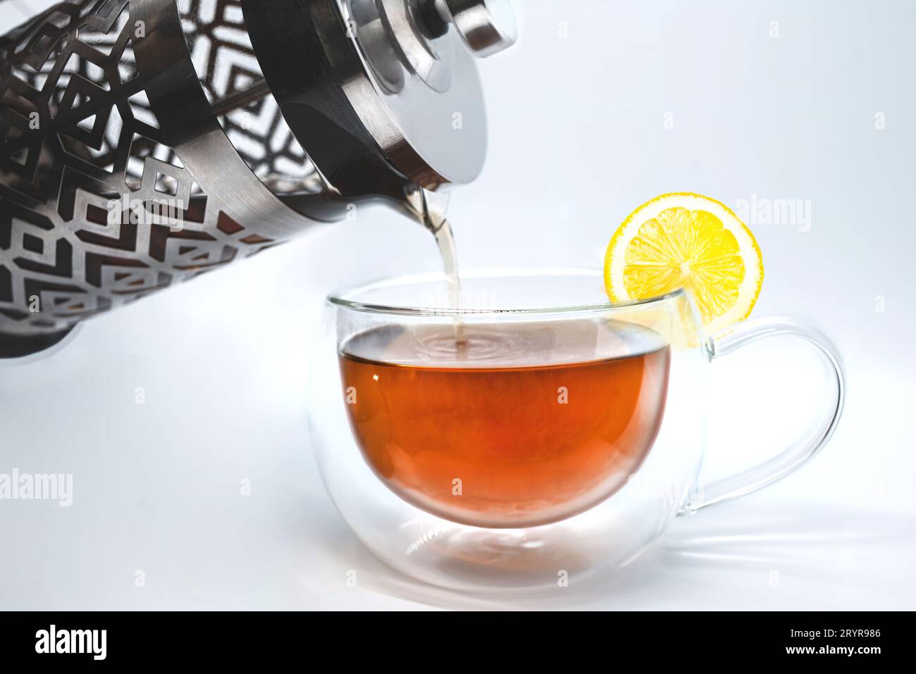 Glass teapot pouring black tea into cup isolated on white Stock Photo