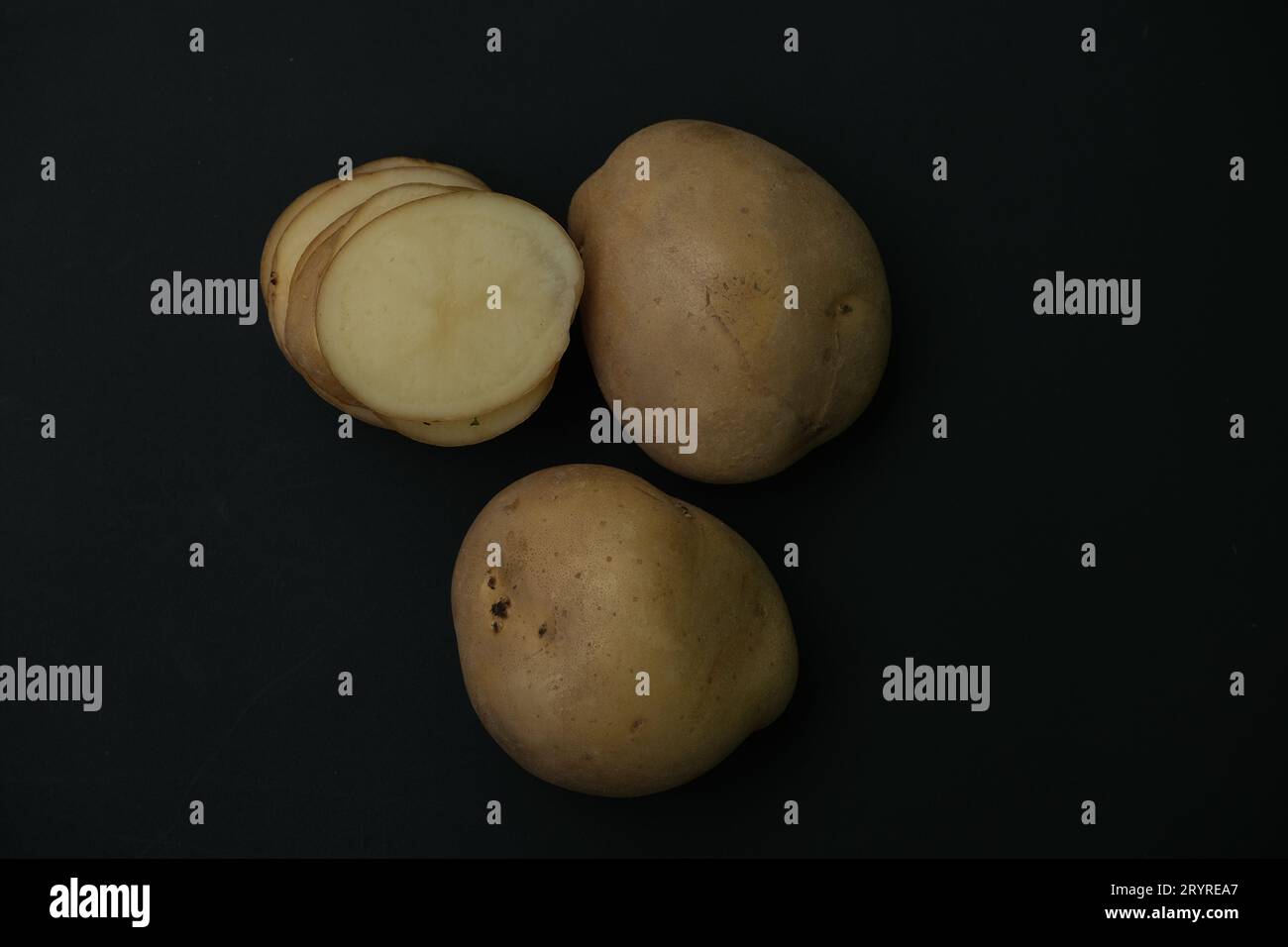 Whole potato and stacked  potato slices on black background. Stock Photo
