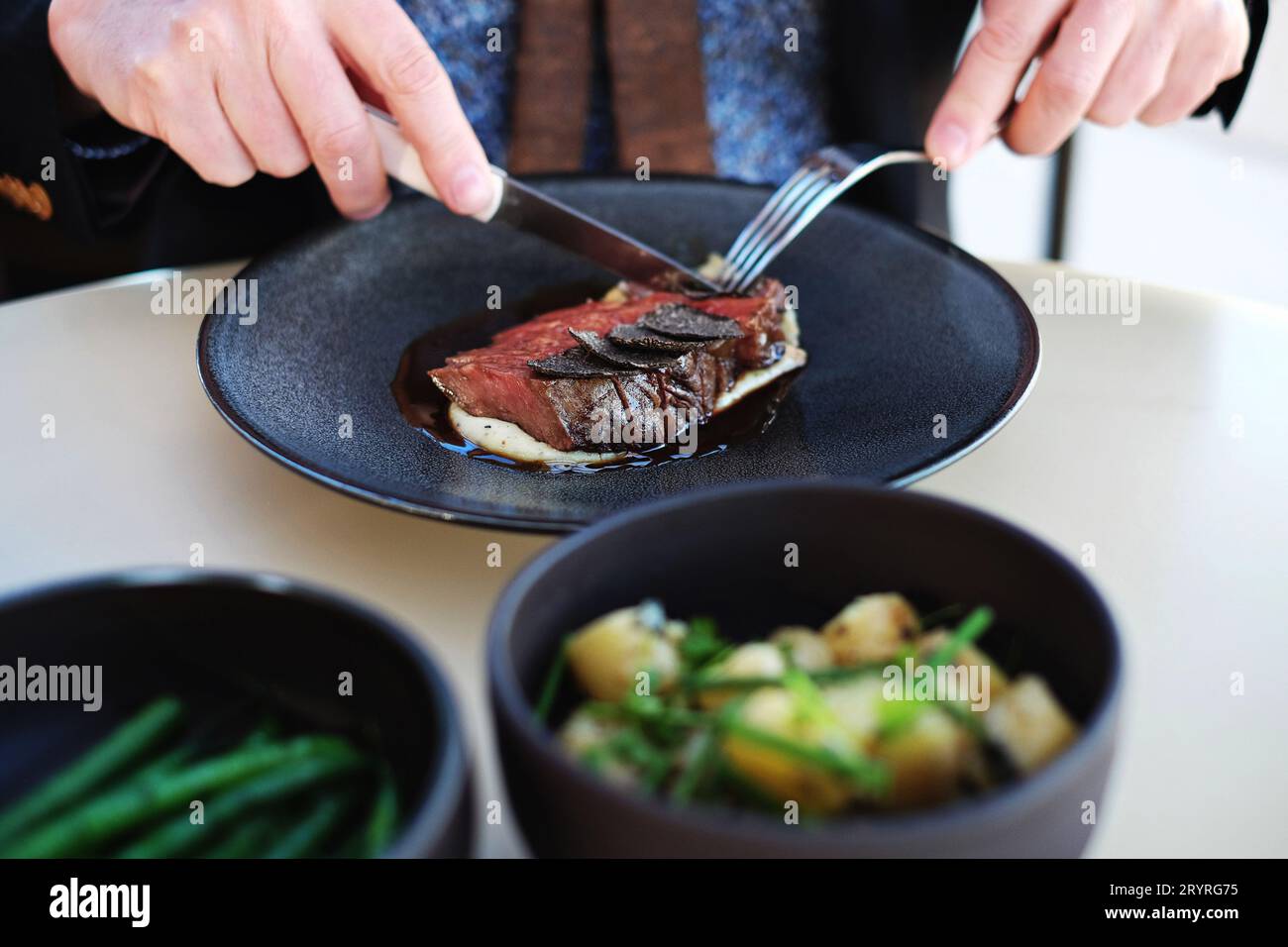 Two hands, knife and fork with a serving o Blackmore Wagyu (9+) with WA