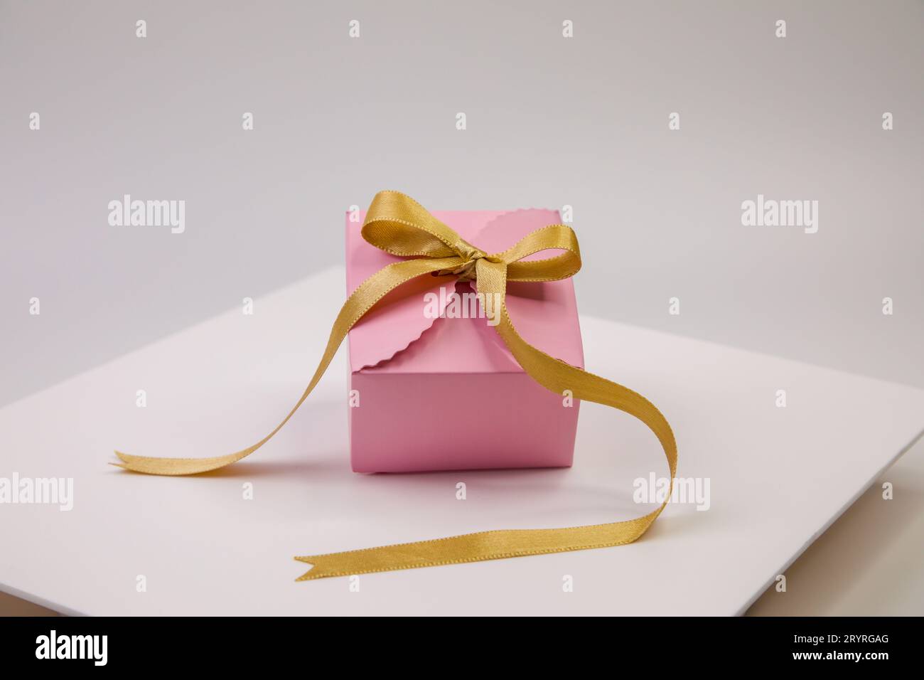 A pink gift box is beautifully wrapped with golden ribbon and sits atop ...