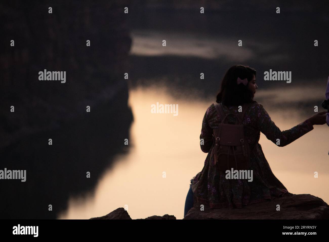 A view from the back of a tourist girl sits on a mountain and admires the beautiful view and dawn or sunset or sunrise. Woman sitting on a rock over m Stock Photo