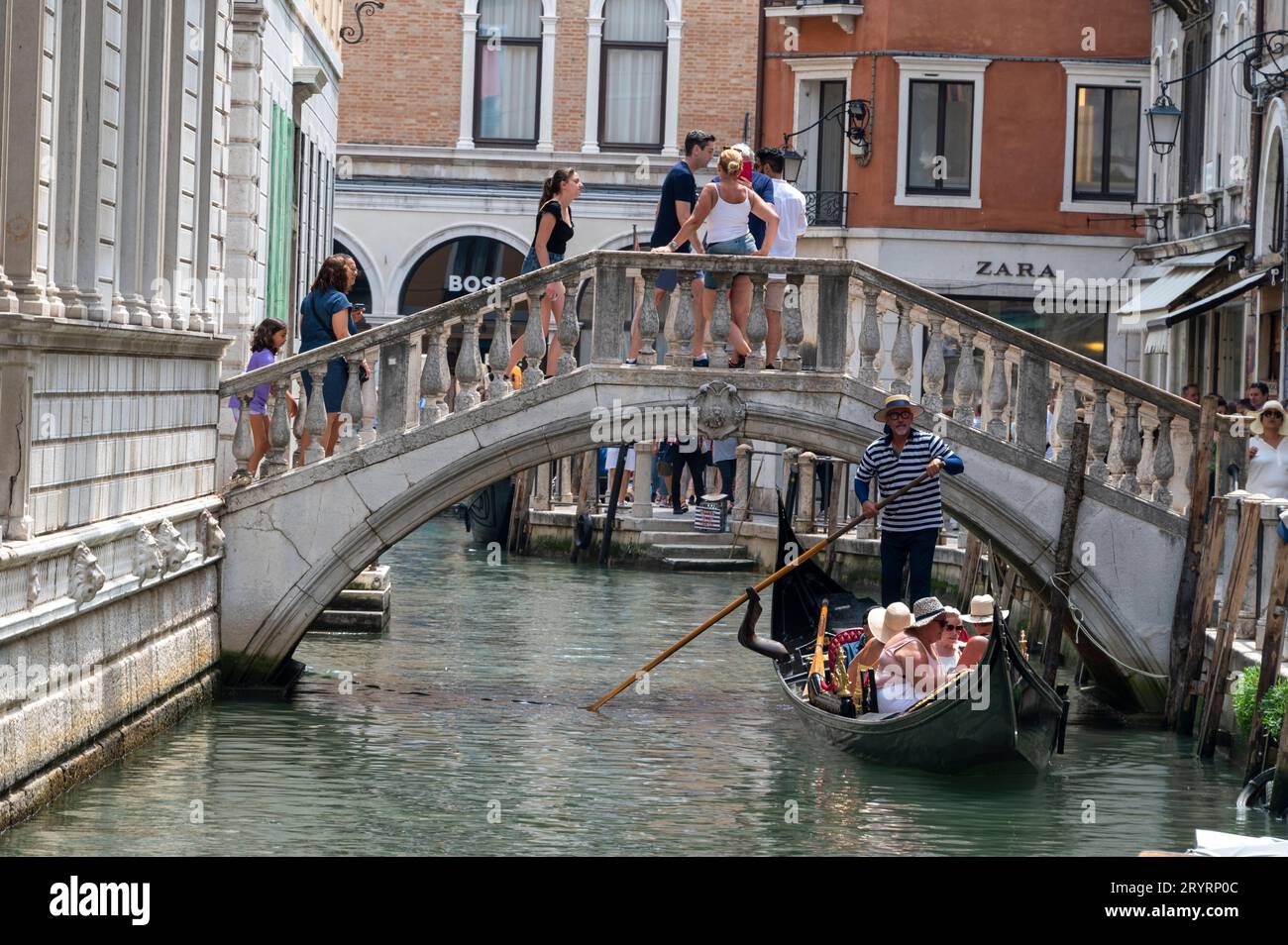 A gondolier steers his gondola under one of the many low footbridges into the Grand Canal close to the Rialto Bridge in Venice in the Veneto region of Stock Photo