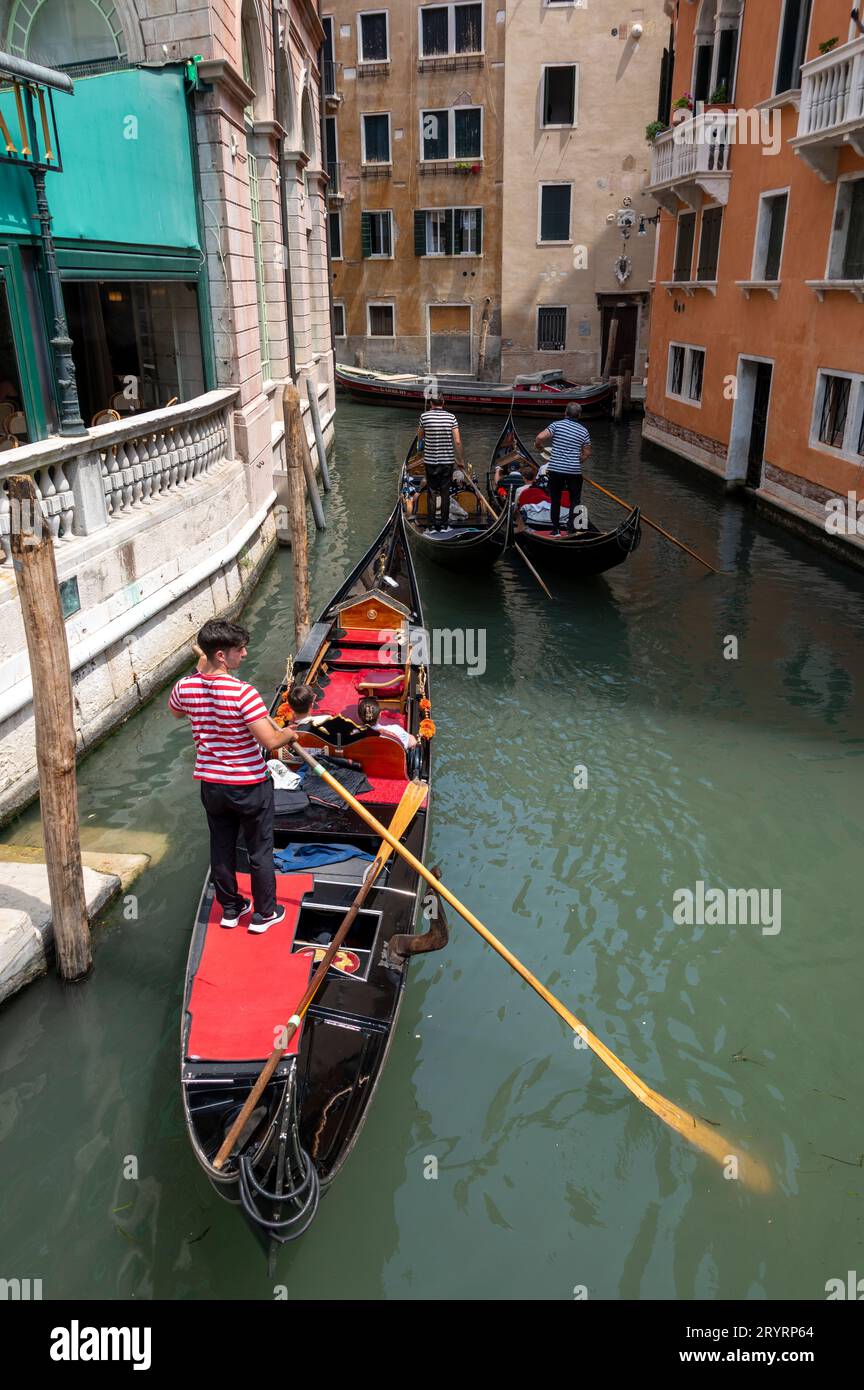 Three gondoliers steer their gondolas in a backwater canal in Venice in