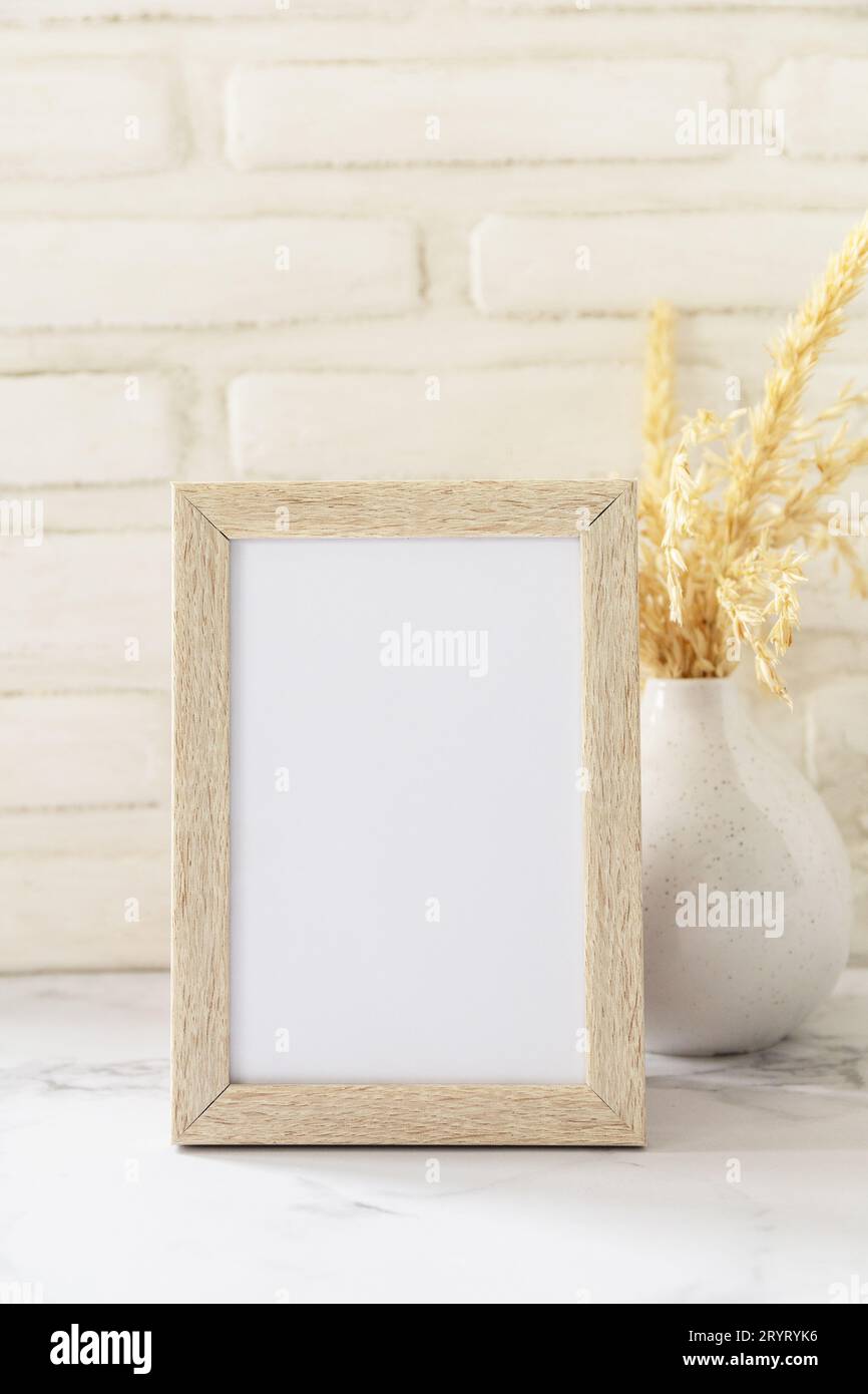 White picture frame mockup. White wall background. Scandinavian interior, neutral color palette with dry grass. Selective focus. Stock Photo