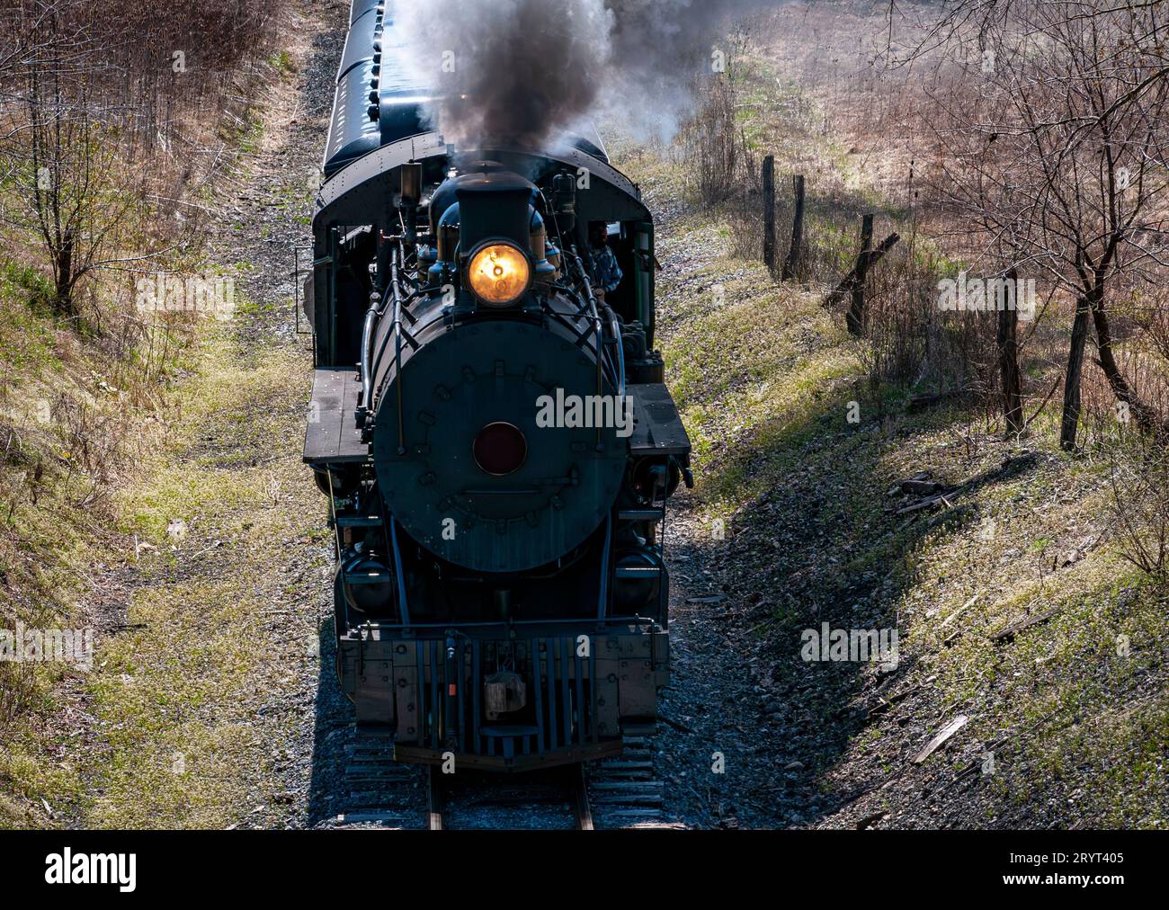 An industrial locomotive in motion, emitting a white plume of steam from its smokestack Stock Photo