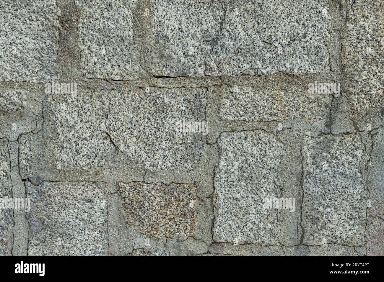 A wall of light granite stones joined with cement between the joints