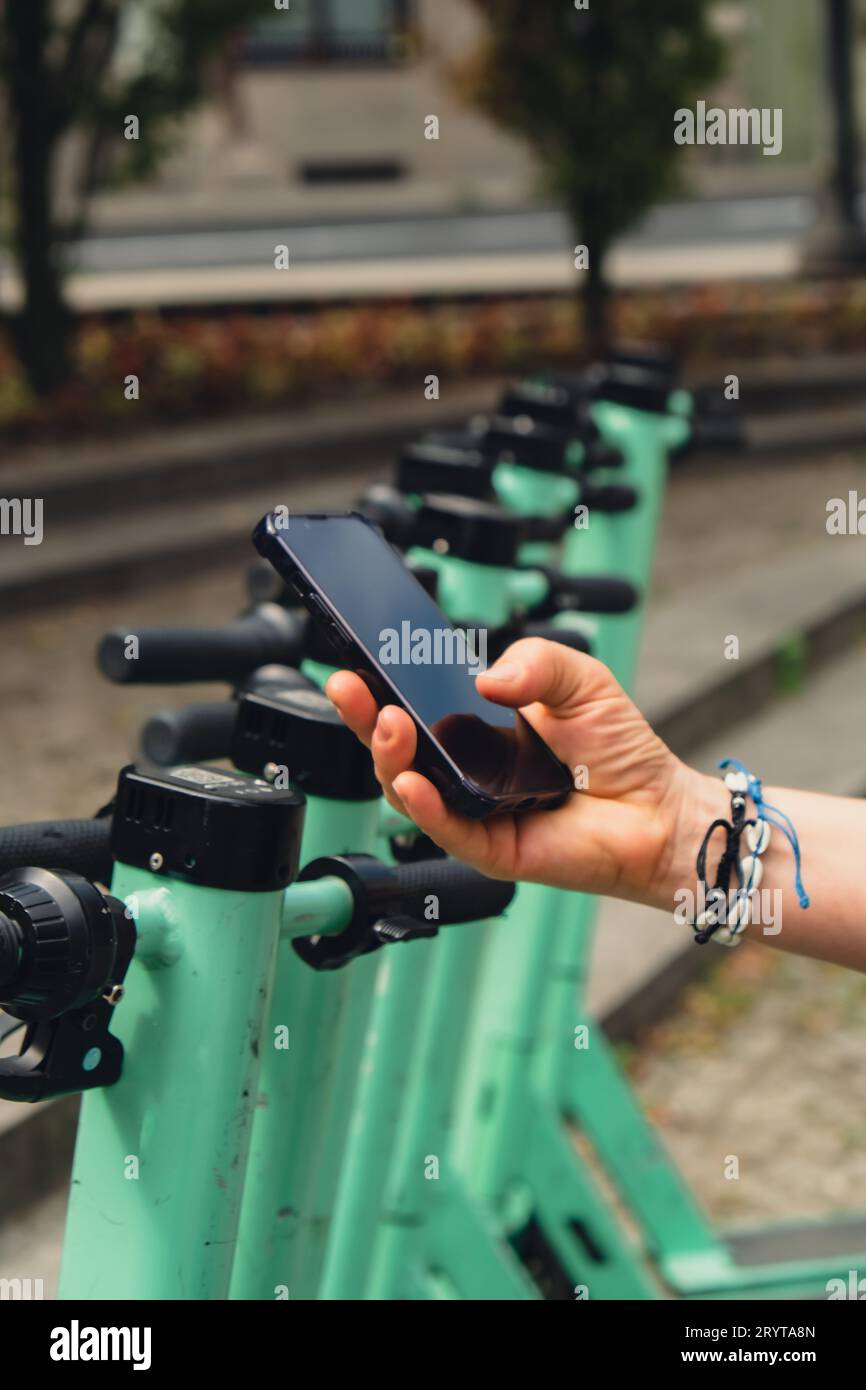 Female hand uses mobile phone to scan QR code on Electric scooter on the street on e-scooter, rental service app. Alternative tr Stock Photo