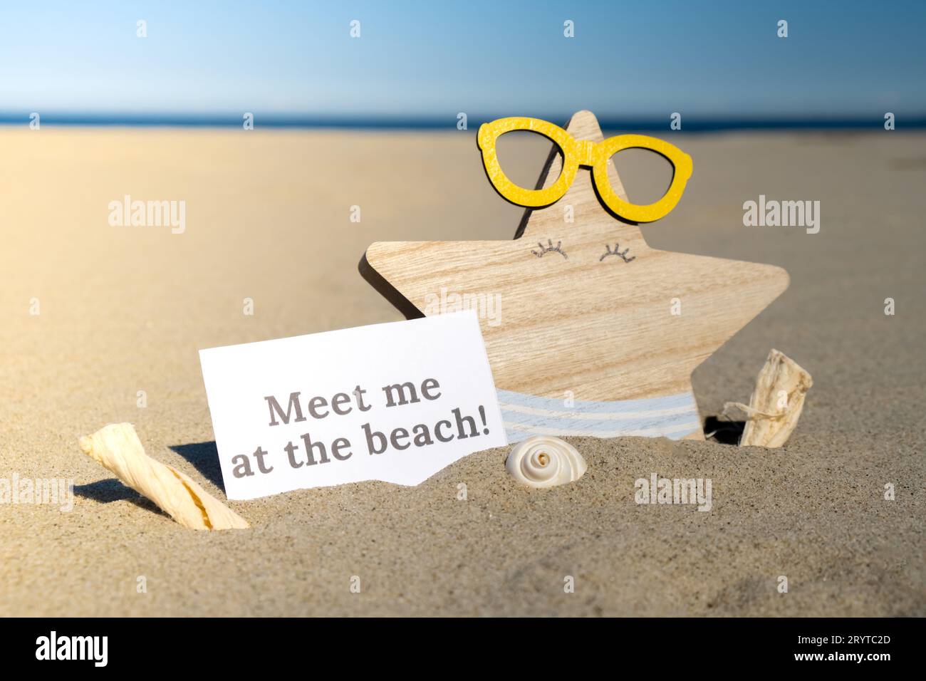 MEET ME AT THE BEACH text on paper greeting card on background of funny starfish in glasses summer vacation decor. Sandy beach s Stock Photo