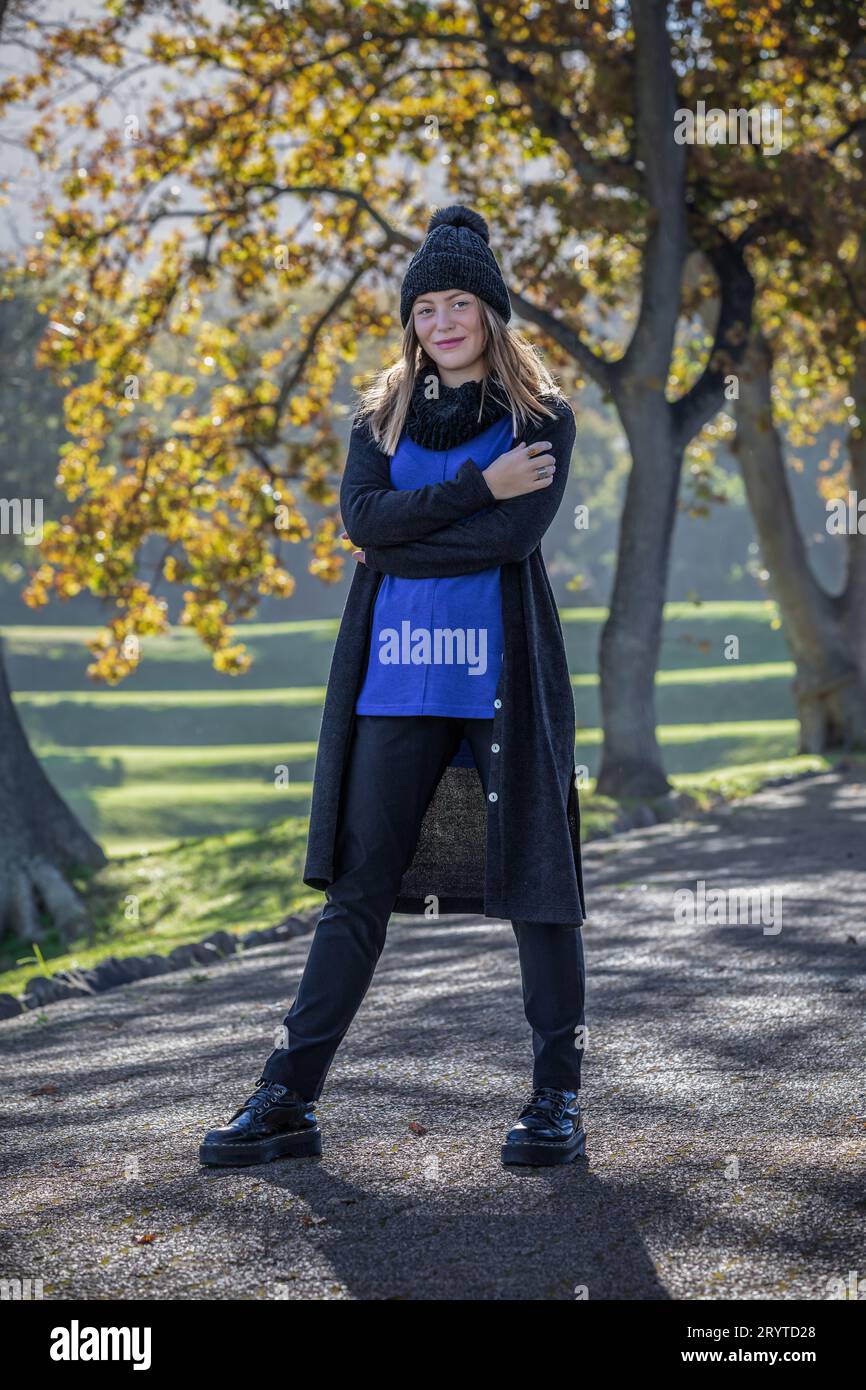 A self assured woman dressed in cozy autumn attire stands amidst the vibrant foliage of big trees adorned with autumn leaves Stock Photo