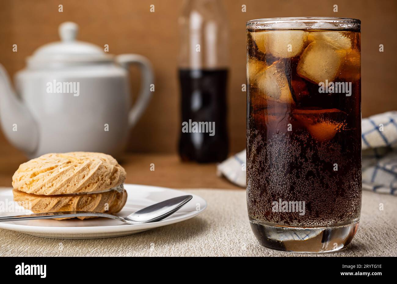 Cold cola water with ice cubes and small round cake filled with blueberry cream. Stock Photo