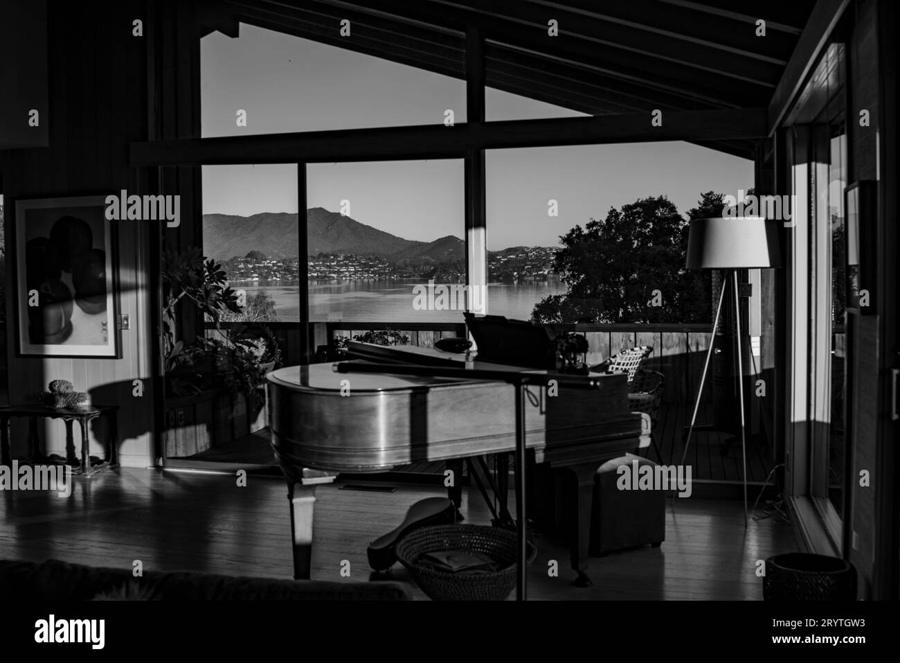 A grayscale shot of a spacious living room featuring a grand piano in the center of the room Stock Photo