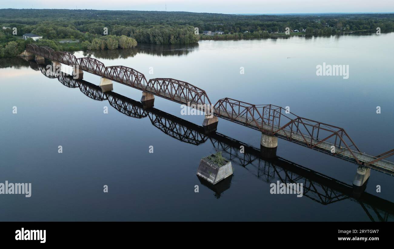 A scenic shot of a bridge spanning a tranquil body of water, with lush greenery in the background Stock Photo