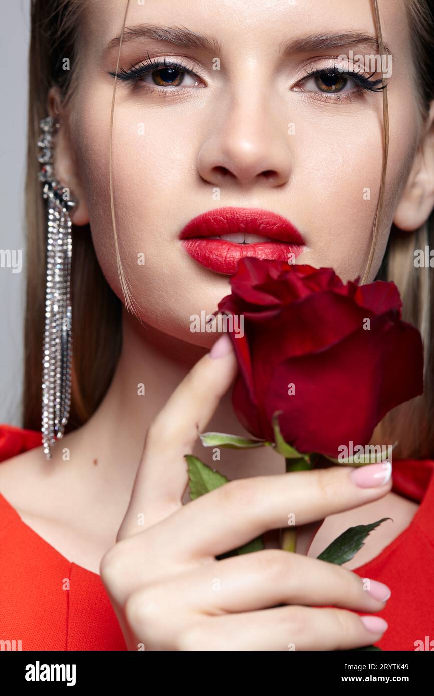 Portrait of young woman in red dress and red rose in hand. Stock Photo