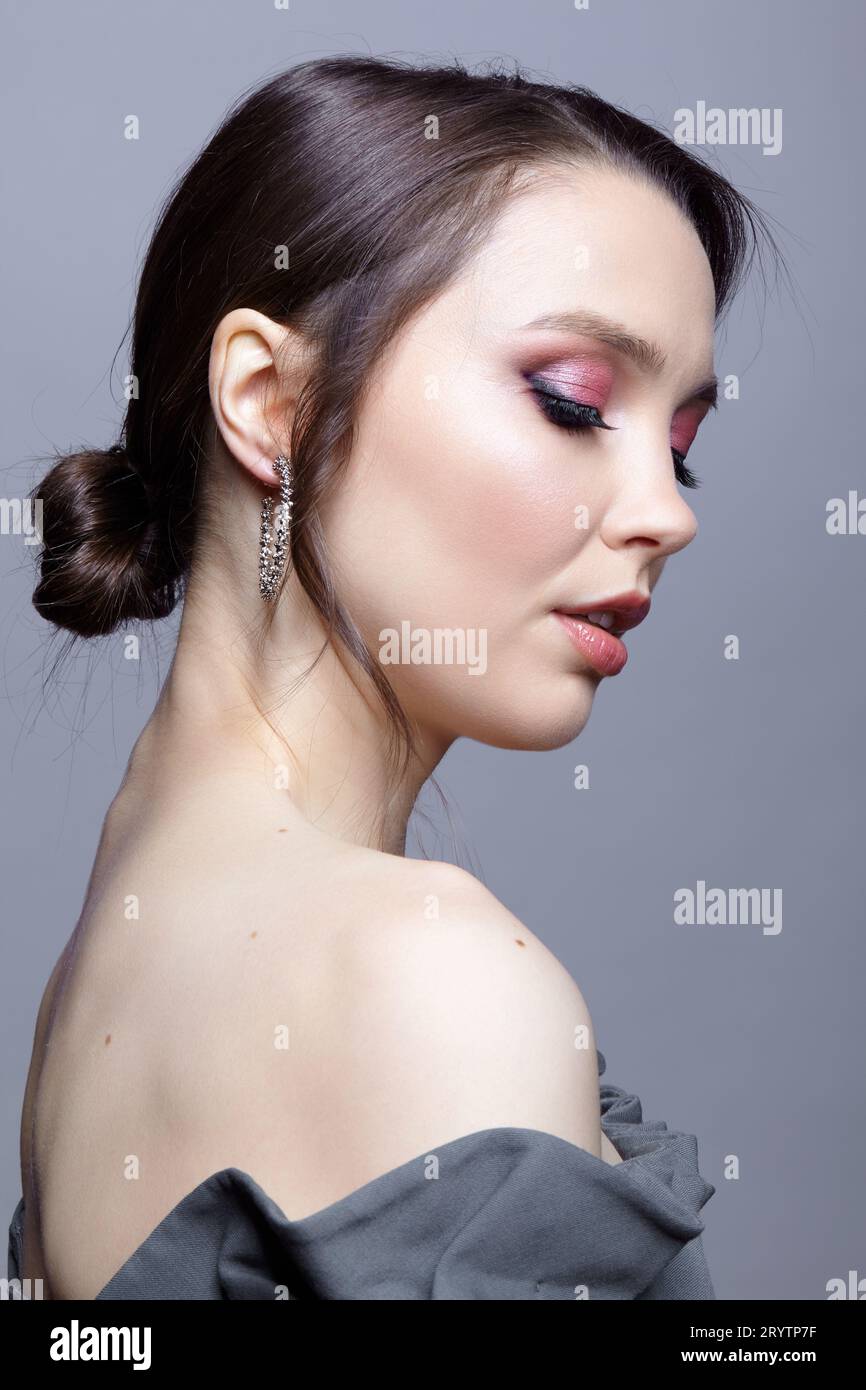 Portrait of young woman in gray dress. Bunette female with hair knot and earring in the ear. Stock Photo