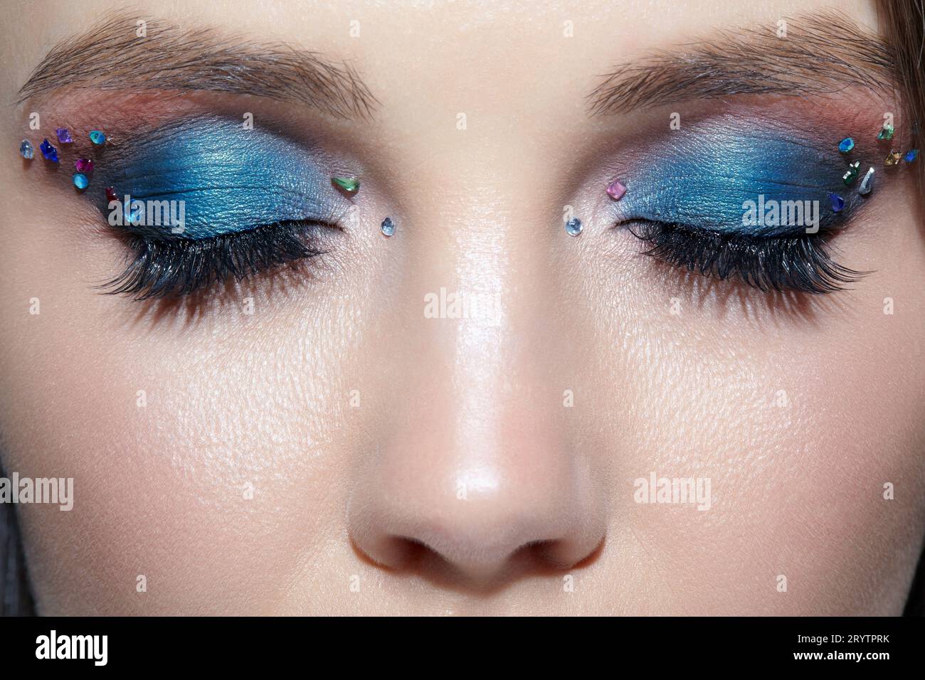 Closeup shot of human woman face with eyes closed and beauty makeup with blue eye shadow make up and rhinestones Stock Photo
