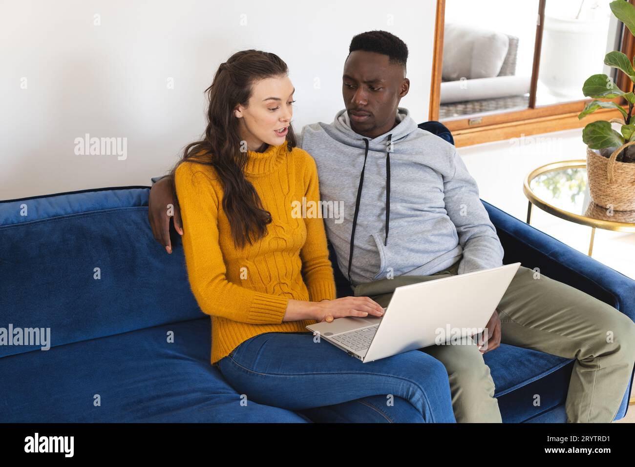 Diverse couple sitting on sofa using laptop at home Stock Photo