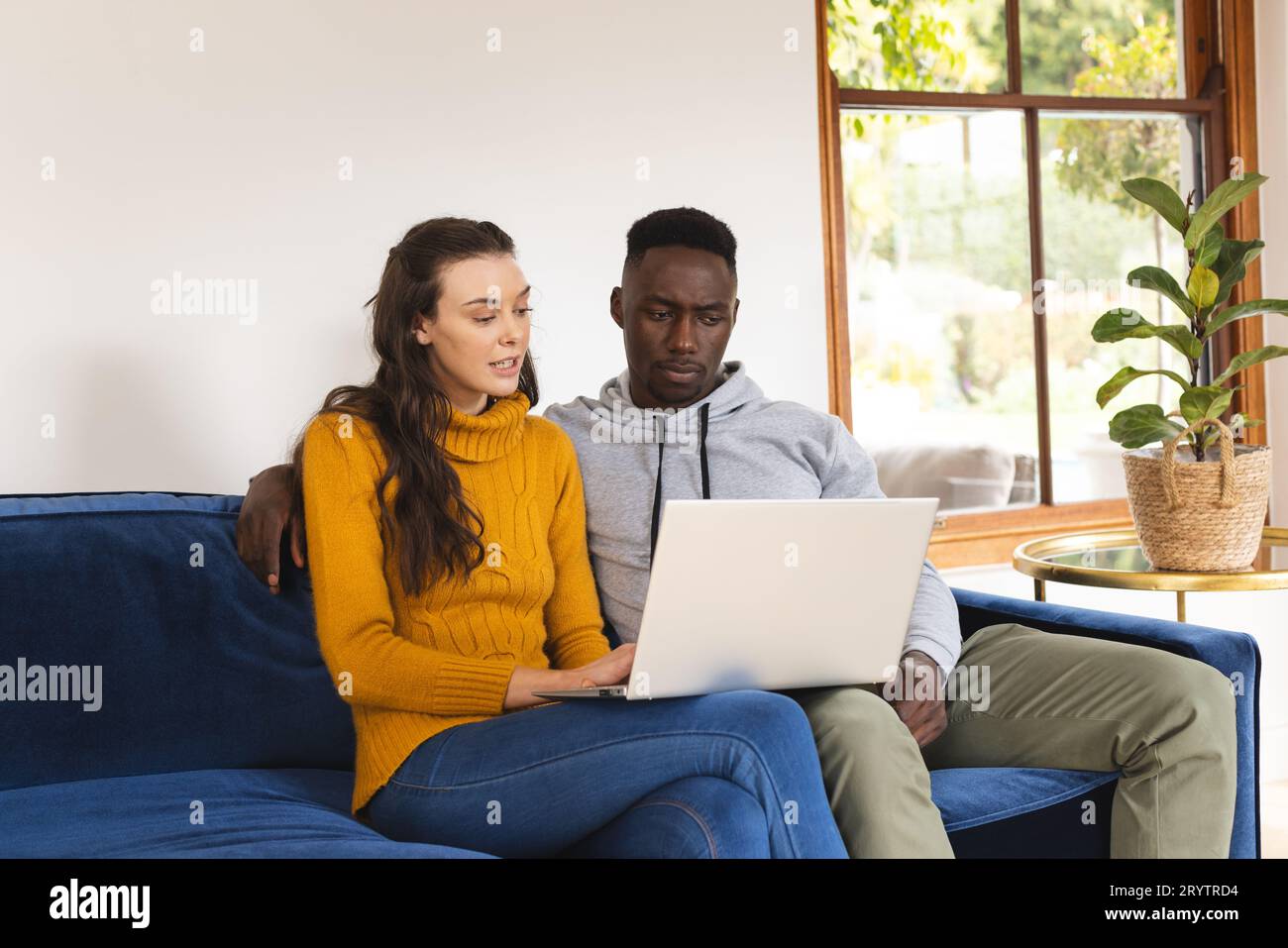 Diverse couple sitting on sofa using laptop at home Stock Photo