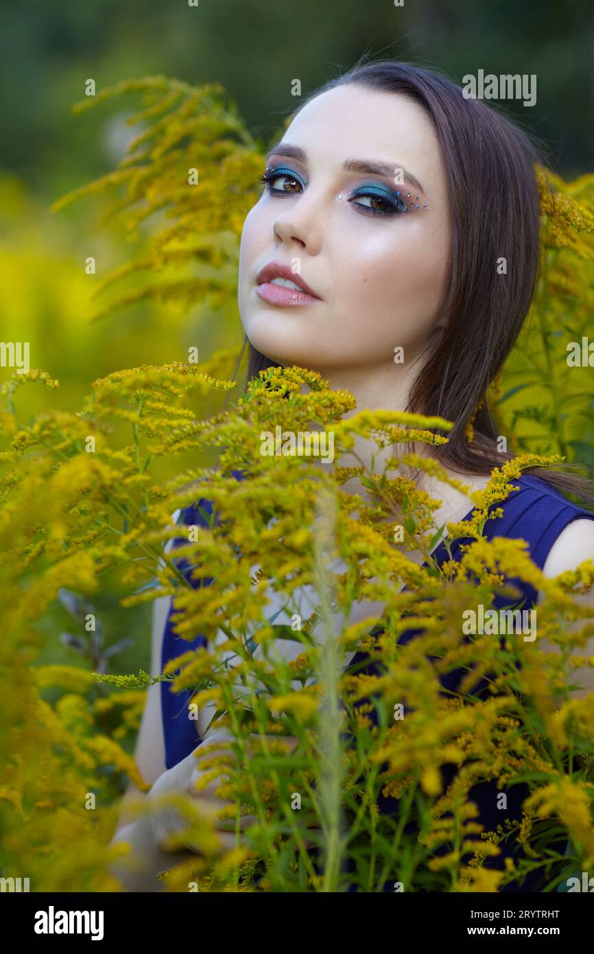 Portrait of brunette woman in the field of yellow Solidago canadensis flowers. Stock Photo