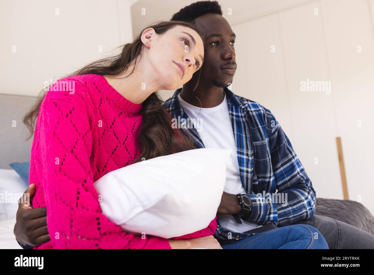Sad diverse couple sitting on bed and embracing at home Stock Photo