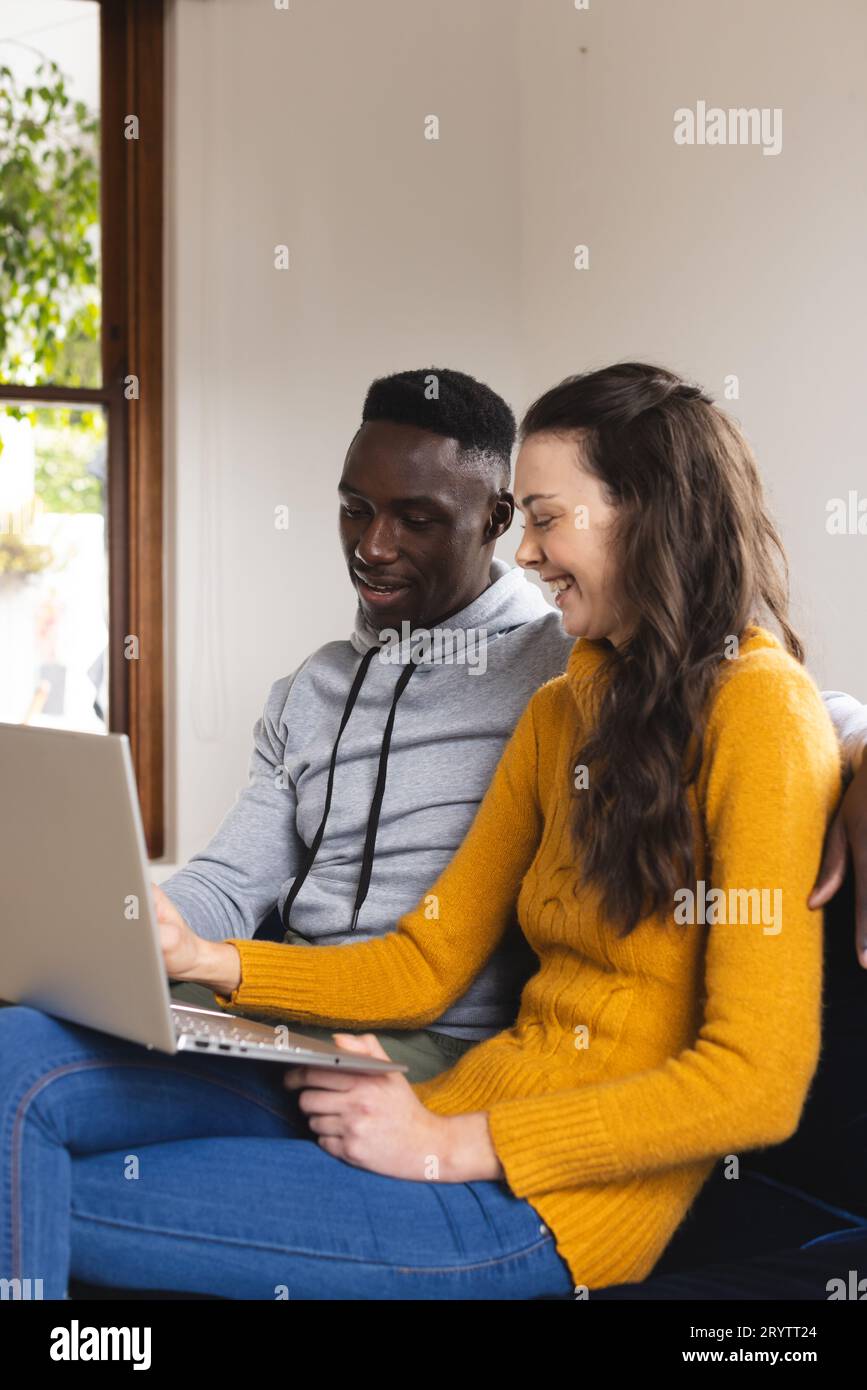 Happy diverse couple sitting on sofa using laptop at home Stock Photo ...