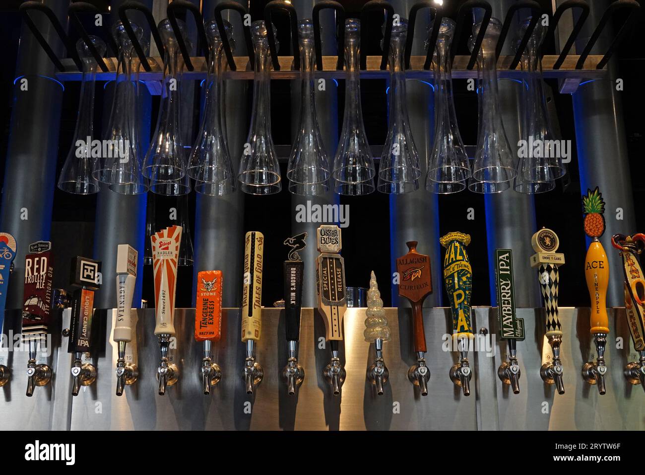 L.A., California, USA - Sept. 15, 2023: A variety of craft beer tap handle logos are shown on display at a bar, with half yard beer glasses above. Stock Photo